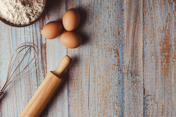 overhead shot on weathered wooden work table with eggs, whisk, rolling pin, flour. Copy space on the right