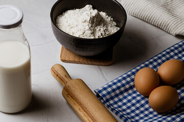 White marble table with bowl of flour, rolling pin, fresh eggs and milk