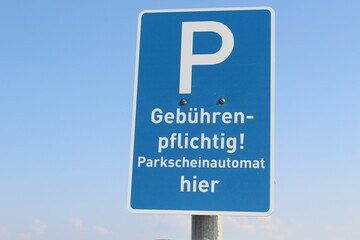 Verkehrsschild Parkplatz vor blauem Himmel: Für das Parken muss man zahlen. Es gibt einen Parkscheinautomat. 