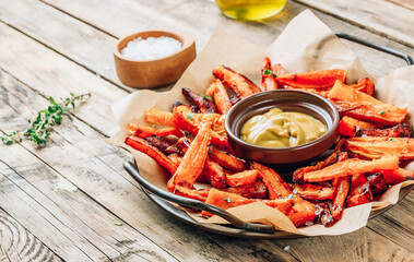 Sweet potato fries on a metal tray with mustard sauce on wooden rustic background.