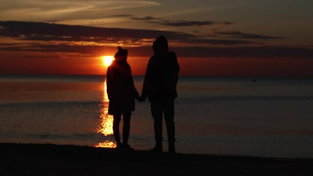 romantic couple in sunset ocean or sea dark time, holding hands walking, standing on seashore coastline. lovers dreaming future, looking sunset in sea, talking. 