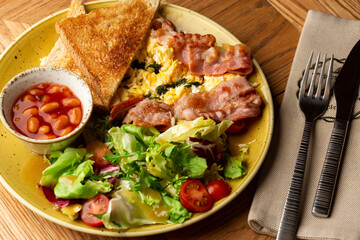 Poached eggs with vegetable, ham, tomatoes, red beans and sourdough toast isolated on wood background. Homemade food. Tasty breakfast.