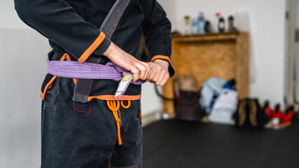 Close up on midsection of unknown bjj brazilian jiu jitsu athlete tie up purple belt on the kimono gi uniform at the academy jiujitsu training concept copy space