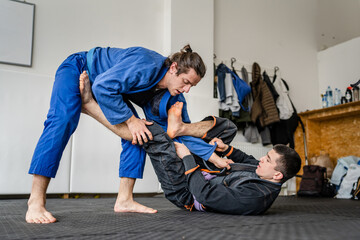 Two brazilian jiu jitsu BJJ athletes training at the academy martial arts ground fighting sparring wear kimono gi sport uniform on the tatami mats sports jiujitsu and self-defense concept copy space