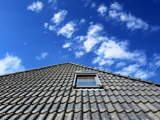 Open roof window in velux style with black roof tiles.