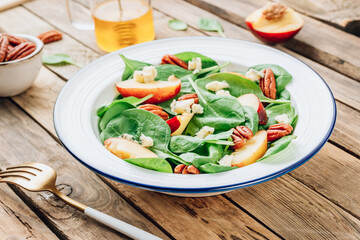 Healthy summer salad with spinach, peach, pecan nuts, blue cheese on wooden table