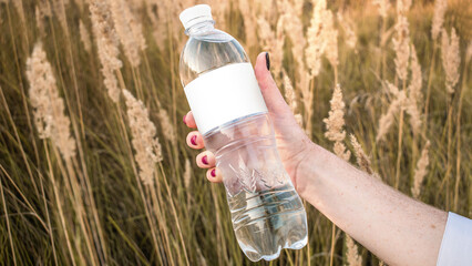 A plastic bottle of water in a girl's hand on a background of grass