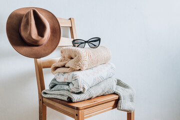 Stack of cozy winter sweaters and hat on the chair on a white background