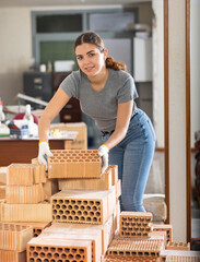 Positive girl in casual clothes stacking red bricks in her apartment during renovations