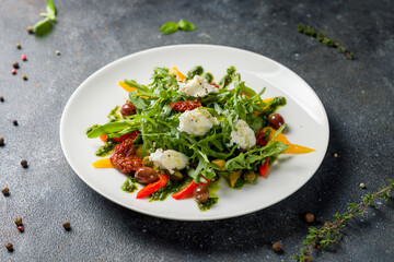 Green vegetable salad with pepper, aragula, sundried tomatoes and cheese with pesto sauce on dark stone table