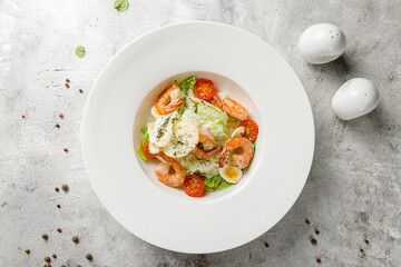 salad caesar with shrimps on white plate on concrete table top view