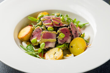 Nicoise with tuna and baby potatoes on white plate on dark stone table macro close up