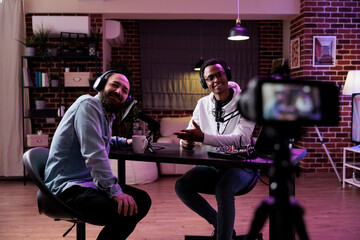 Male influencer using camera to record podcast conversation, filming talking show discussion in...