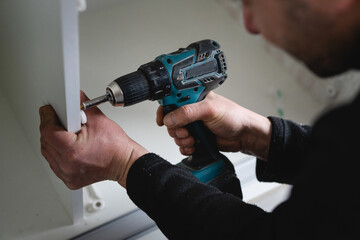 One man caucasian male using electric cordless screwdriver drill assembling furniture at home DIY carpenter at work