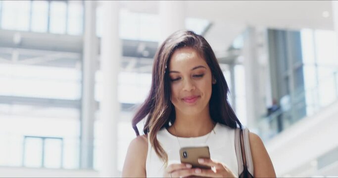 Shell let nothing stand in the way of her success. 4k video footage of a young businesswoman using a cellphone while walking in a modern office.