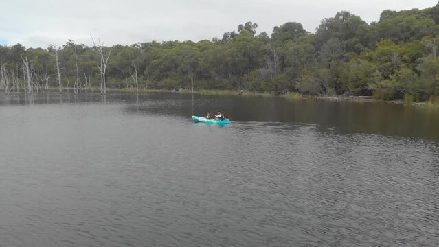 Aerial shot orbiting around a man and his daughter in a blue kayak paddling on a lake in baw baw country Australia.
