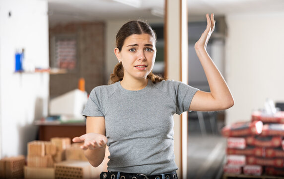 Puzzled young woman examining room in her house during unfinished renovation works indoors..