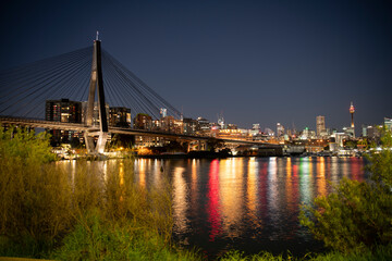 Anzac Bridge from Blackwattle Bay, Glebe, Sydney, Australia at night with Sydney city skyline. Colourful building lights reflect in the bay water.