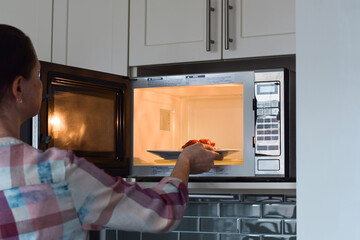 Woman placing plate with food into microwave to warm up