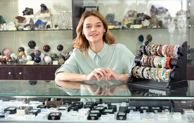 Portrait of cheerful female shop assistant demonstrating jewelry made of natural stones