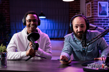 POV of male influencers recording podcast chat on camera, using streaming equipment in studio with neon lights. Content creators having fun filming online episode for social media. - obrazy, fototapety, plakaty