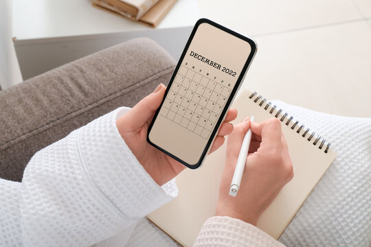 Woman with modern mobile phone using calendar application at home