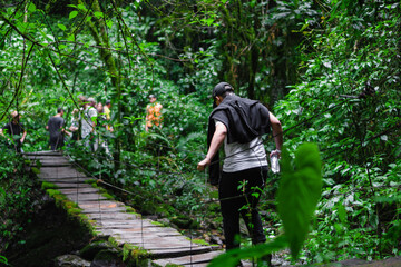 young latin man in the jungle crossing a wooden suspension bridge, ecological hike, environmental...