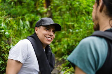 Naklejka na ściany i meble young latin man in the jungle smiling while talking to his hiking partner