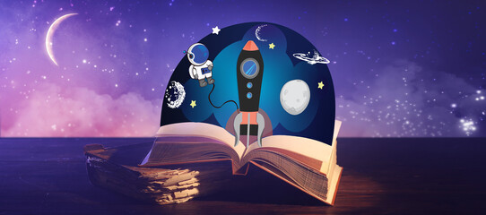 Old books with drawn spaceship on table against sky at night