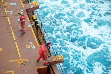 Fotobehang Seaman ship crew priming and derusting vessel deck for upcoming painting. © Denys Yelmanov 