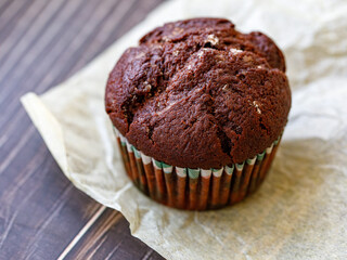 One homemade freshly baked delicious chocolate muffin served on baking paper on dark wooden table, closeup, side view. Fresh handmade pastry. DIY. Copy space for text