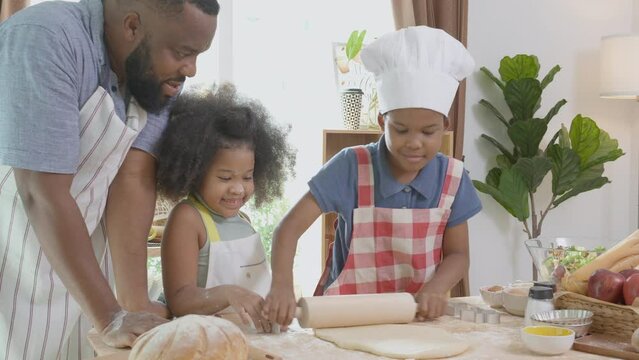 African American family with son and daughter rolling for thresh flour for cooking with father together in the kitchen at home, parent and little child activity preparing food with fun.
