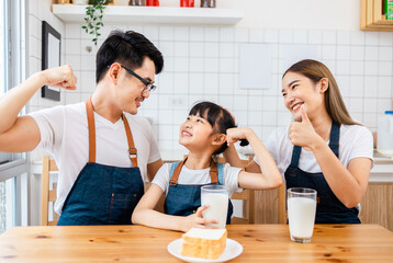 Asian  family enjoying breakfast at cozy kitchen, little girl daughter sitting on table, drinking...