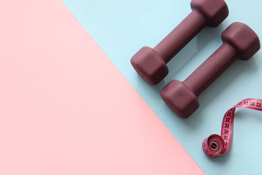 Stylish dumbbells and measuring tape on color background © Pixel-Shot