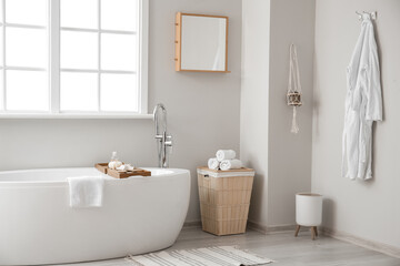 Interior of light bathroom with mirror, basket and bathtub