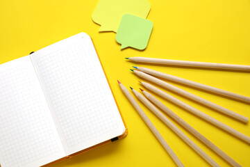 Blank notebook and colorful pencils on yellow background
