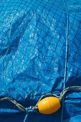 Yellow fishing float and rope on bright blue plastic sheet