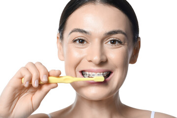 Obraz na płótnie Canvas Beautiful woman with dental braces brushing teeth on white background, closeup