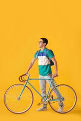 Male Asian student with bicycle on yellow background