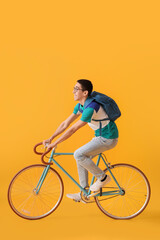 Male Asian student riding bicycle on yellow background