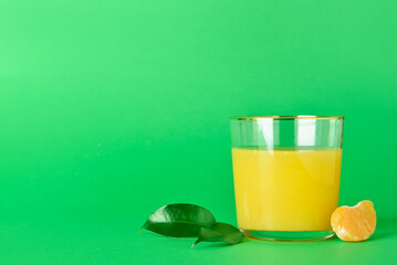Glass of fresh tangerine juice on green background