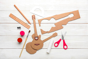 Cardboard guitar toy with materials on white wooden background