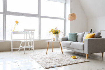 Vase with mimosa flowers on table and sofa in interior of living room
