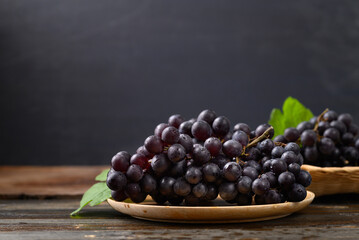 Red grape on wooden plate with black background