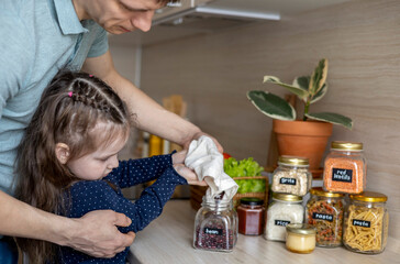 Dad and daughter pour cereal from a reusable bag into a glass jar. Storage in the kitchen.