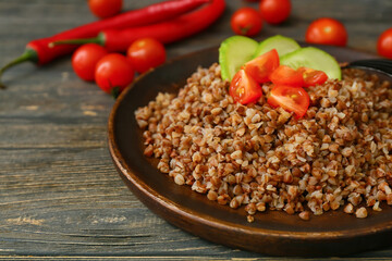 Plate of tasty buckwheat porridge with vegetables on wooden table, closeup