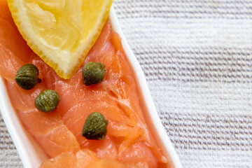 Fresh smoked salmon and capers with lemon on a white plate.