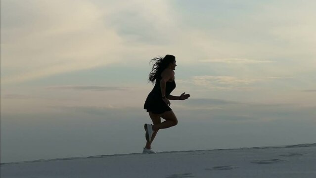 Young active woman running  in the desert at sunset. Slow motion footage of a young woman in a black short tracksuit running through the desert. Feeling of freedom concept. Sports lifestyle.