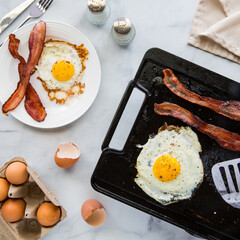 Top down view of a griddle pan cooking bacon and eggs for breakfast.
