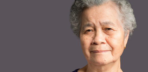 Senior woman with short gray hair looking at the camera with a smile while standing on gray background